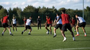 Football players moving together in a coordinated training drill while a coach observes