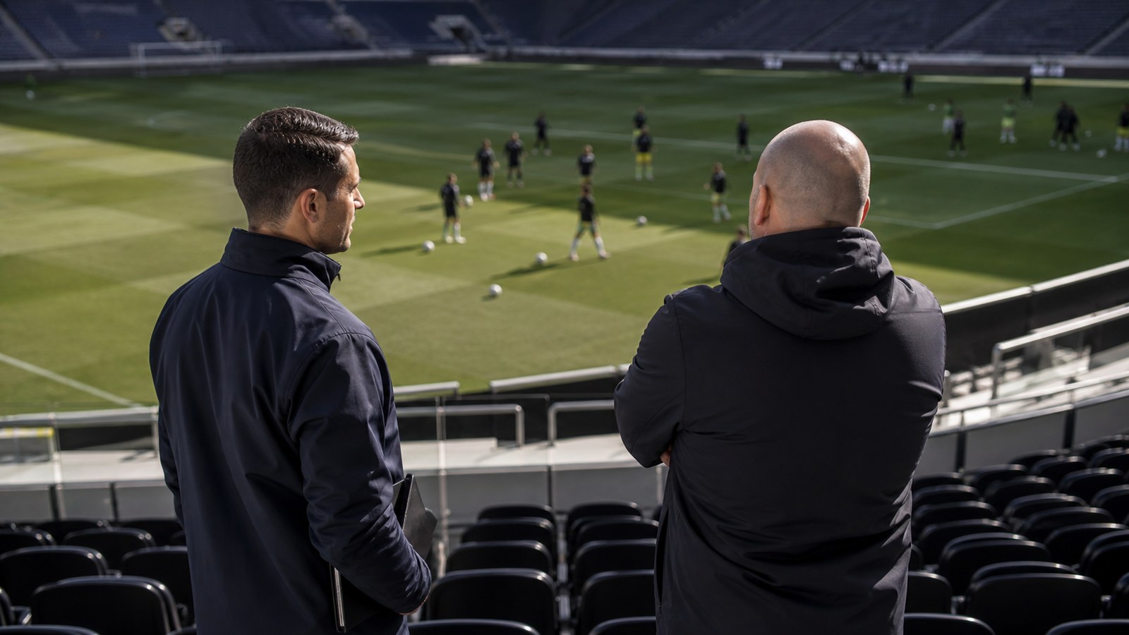 Soccer coaching staff watching an opponent warm up from the stands before kickoff